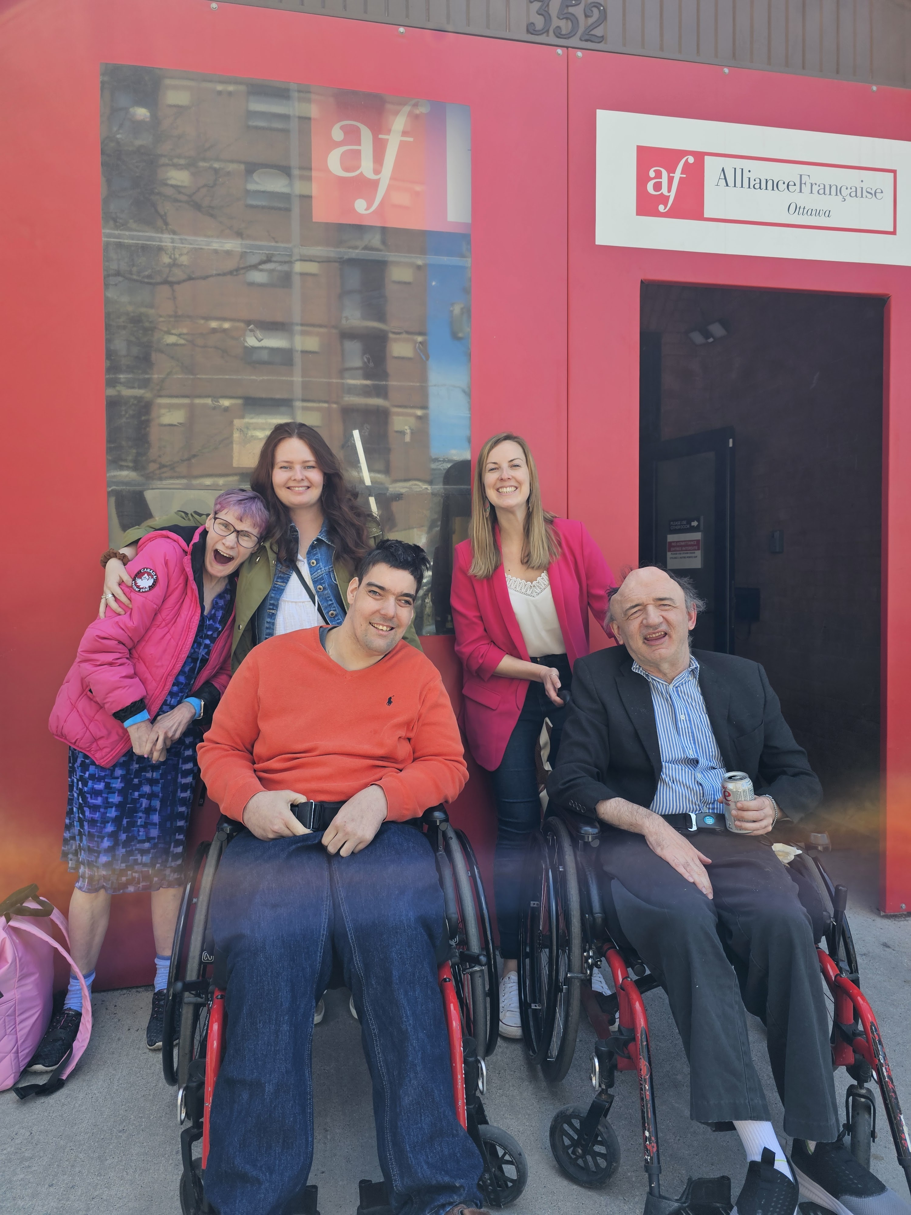 des membres de cœur et les assistants posent en avant d'un bâtiment rouge.