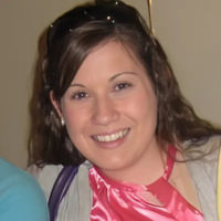 Femme portant une chemise rose, posant pour l'appareil photo avec des lunettes de soleil sur la tête et tirant ses cheveux en arrière.