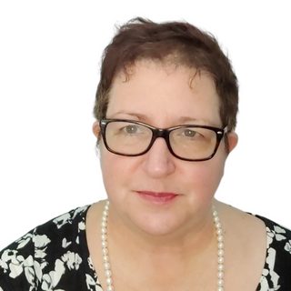 Une photo d'une femme posant devant un fond blanc, portant une chemise à motifs noirs et blancs et des lunettes.